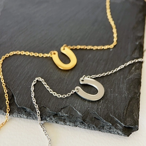 Polished gold and silver horseshoe pendants on thin chains over a grey stone surface