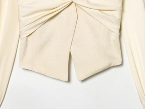 Dettaglio dell'elegante camicia crema con nodo a torsione e orlo asimmetrico sotto