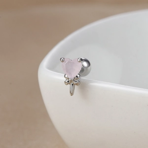 Macro view of a silver heart stud earring with pink gemstone and metal bow detail