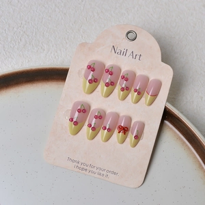 Detail of French style press-on nails with 3D cherry and red bow on textured card