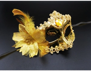Detail of gold masquerade mask featuring yellow feathers, fabric flower and amber gemstone