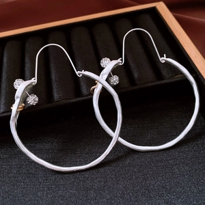 Macro detail of silver twisted hoop earrings with rhinestone accents on a black display