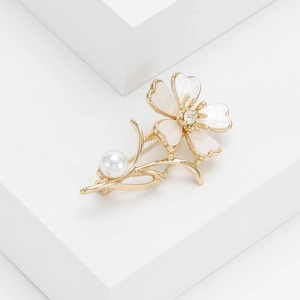 Detail of a golden flower brooch with white enamel petals and a center crystal pearl