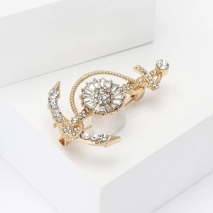 Golden ship anchor and helm brooch with rhinestones on a white geometric stand