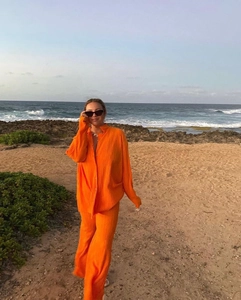 Close-up of pleated orange long-sleeve shirt and wide-leg pants set on a beach background