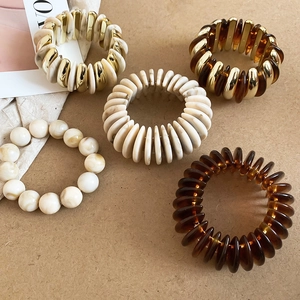 Detail of 5-piece set acrylic bead bracelets and resin spiral bands in amber and beige