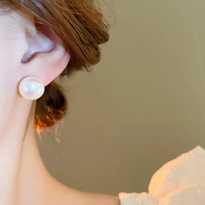 Detail shot of elegant mermaid pearl stud earring with gold plating on model's ear