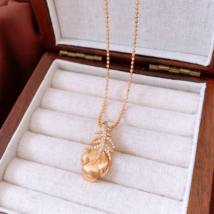 Close-up of 18k gold plated feather pendant necklace on white cushion in wooden jewelry box