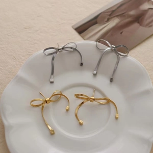 Detailed close-up of gold and silver bow knot tassel earrings on a white floral plate