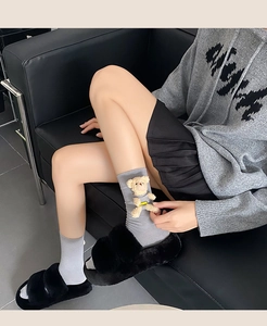 Close-up of grey mid-calf socks with 3D plush bear detail and black fuzzy slides