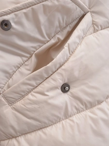 Detailed macro view of quilted beige padded jacket showing the pocket and fine stitching
