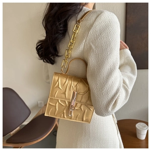 Detail of gold textured crossbody bag with metal chain strap and elegant clasp lock
