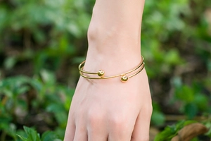 Close-up of a gold open bangle with two spherical beads worn on a wrist outdoors