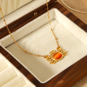 Golden stainless steel necklace with orange cat's eye crab pendant in a wooden box