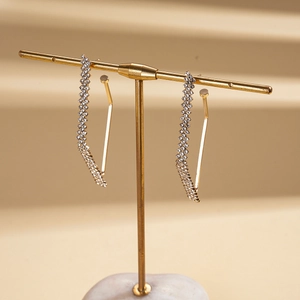 Detail of gold geometric diamond earrings on a minimalist marble T-stand display