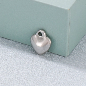 Polished silver heart pendant made of stainless steel displayed on a white textured surface
