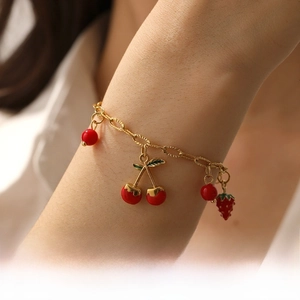 Détail des breloques cerise et fraise sur un bracelet en chaîne dorée porté au poignet