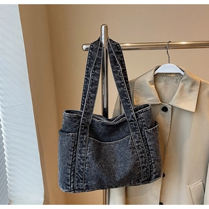 Detail of vintage washed denim tote bag in dark gray hanging against a beige coat