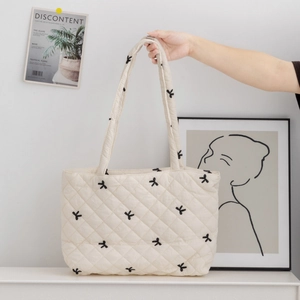 Close-up of cream quilted tote bag featuring black bow embroidery and grid stitching