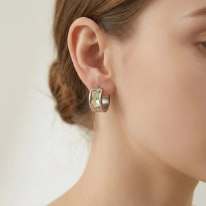 Detailed view of women's stainless steel huggie earring with radiant cut green gemstone
