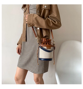 Detailed close-up of canvas bucket bag with brown leather trim and drawstring closure