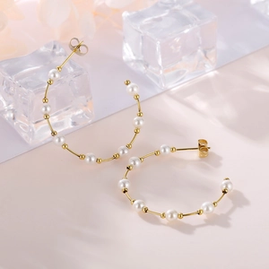 Detailed view of gold C-shaped hoop earrings with pearls on a soft pink background