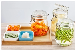 Close-up of glass storage jars with airtight metal buckles and ceramic snack bowls on wood