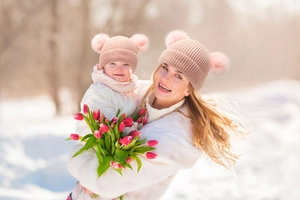 Matching set of mother and baby winter knit beanies with fluffy pink faux fur pom poms