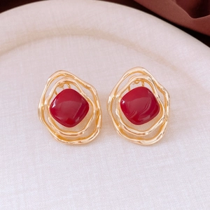 Macro shot of irregular gold earrings with red stones on a beige textured tray