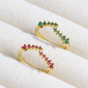 Detail of two gold V-shaped rings with inlaid green and red zircon stones on fabric