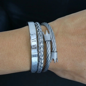 Detailed view of three silver stainless steel bracelets with Roman numerals and crown charm