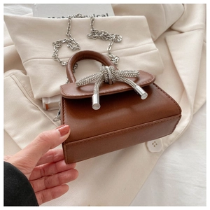 Detail view of brown mini shoulder bag featuring a sparkling diamond-encrusted knot and silver chain