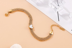 Detailed close-up of a layered gold stainless steel bracelet with a white heart charm