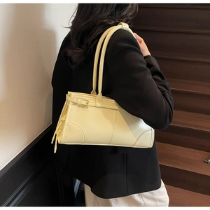 Detail of beige leather shoulder bag with gold hardware and tassel on model in wood stairs