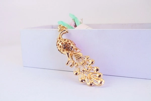 Detail of a golden metal peacock pendant with hollow design on a white gift box