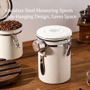 White stainless steel coffee canister with scoop and date tracker on wooden desk