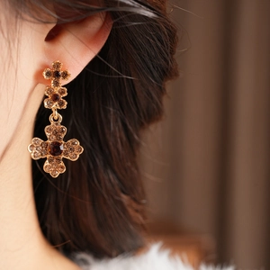 Close-up of vintage gold cross earrings with amber rhinestones on model's ear