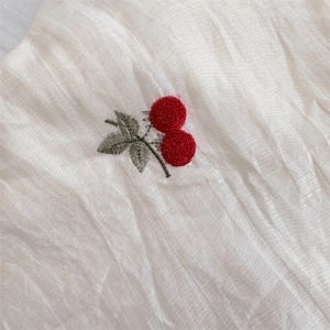 Macro detail of cherry embroidery on white pleated fabric for shoulder bag