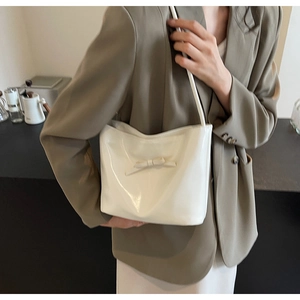 Detail of a beige ribbon shoulder bag with a glossy finish shown on a model