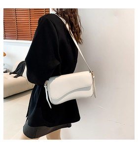 Minimalist white leather crossbody bag with wave edge flap shown on shoulder