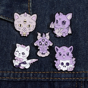 Close-up of five creepy-cute purple enamel cat and devil pins on blue denim fabric