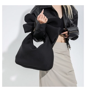 Detail of a large bow decoration on a black neoprene tote bag held by a model