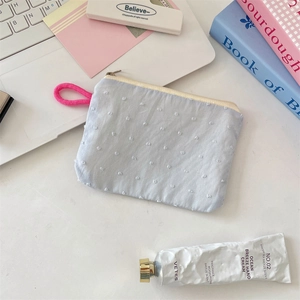 Close-up of light blue textured coin purse with 3D dots and pink lanyard on desk