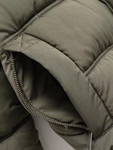 Detail shot of the zipper pocket and olive green quilted fabric on hooded jacket