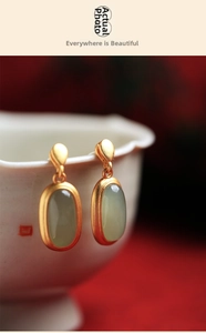 Macro shot of gold-plated drop earrings with green jade inlay on a ceramic cup