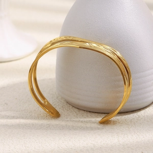 Detail of double-layer gold wavy cuff bracelet on a matte ceramic vase accessory