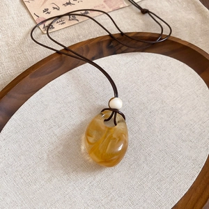 Detailed macro view of amber resin pendant with white bead on a dark brown cord