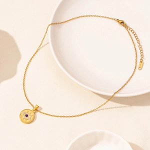 Detail of gold evil eye necklace with blue gem and S.STEEL engraving on the tag