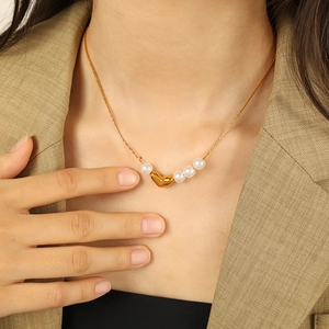 Élégant collier avec pendentif cœur doré et perles porté par un mannequin en blazer