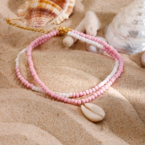 Pink and white beaded ocean style necklace with a natural seashell pendant on sand